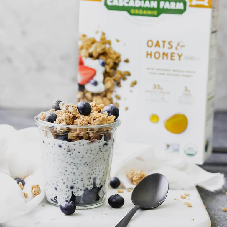 Recipe image of Cascadian-Farm fruit and granola chia pudding in a clear cup with Cascadian Farm Oats & Honey granola, front of box, in the background