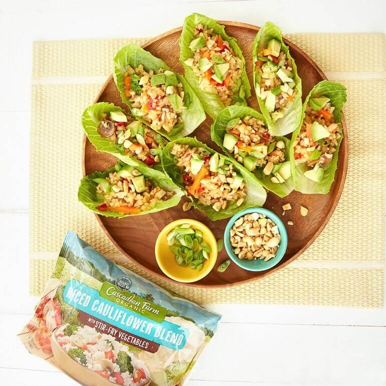 A plate with cauliflower rice filled lettuce leaves, next to a bag of Cascadian Farm Riced Cauliflower, for the recipe