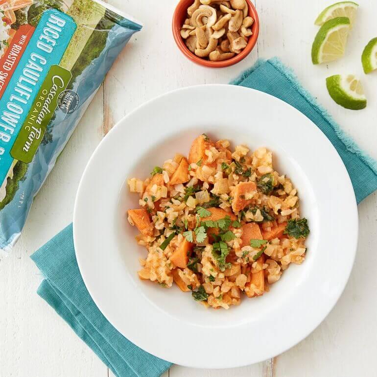 Recipe image of sweet potato red curry next to a bag of Cascadian Farm Frozen Organic Riced Cauliflower Blend and garnishes
